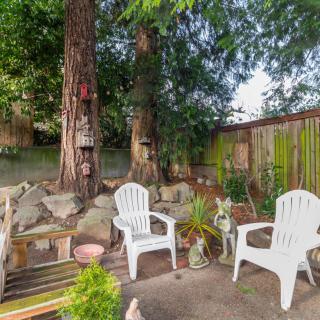A cozy backyard patio with white chairs and lush greenery.