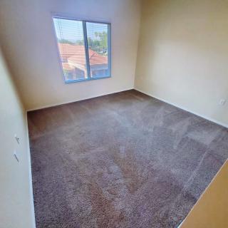 An empty carpeted room with a window and plain walls.