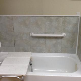 A bathroom featuring a bathtub with a grab bar for accessibility and safety, surrounded by tiled walls.