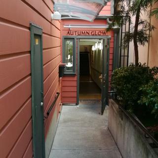 A narrow alleyway leading to a doorway with an overhead entrance sign and surrounding greenery.