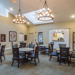 A well-lit dining area with elegant chandeliers, tables, and chairs arranged for seating.