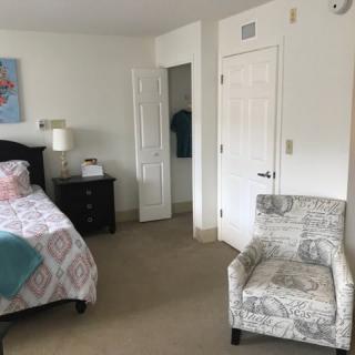 A minimalist bedroom with a bed, armchair, nightstand, and an open door.