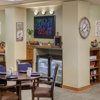 A cozy dining area with elegant table settings and stylish decor, featuring a wall clock, artwork, and mini refrigerators.