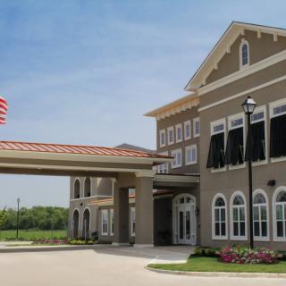 A modern building with an entrance canopy and an American flag, surrounded by landscaped gardens on a sunny day.