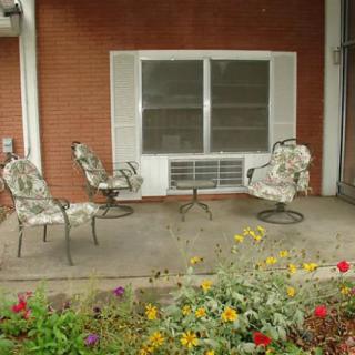 A cozy patio with floral chairs and a small table surrounded by blooming flowers.