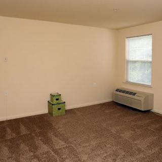 An empty room with brown carpet, a window, two green boxes, and an air conditioner.