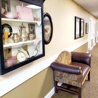 A hallway with a display case of antiques and a vintage chair along the wall.