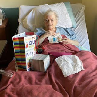 An elderly person in a hospital bed surrounded by gifts.