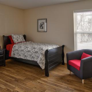 A minimalist bedroom with a single bed and a comfortable chair on a wooden floor.