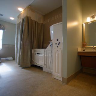An accessible bathroom featuring a walk-in tub with curtains, tiles, and a mirrored vanity area.