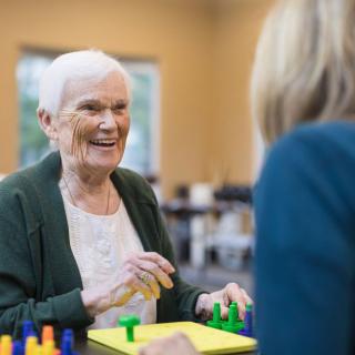 An elderly woman smiling while engaging in a leisure activity indoors.