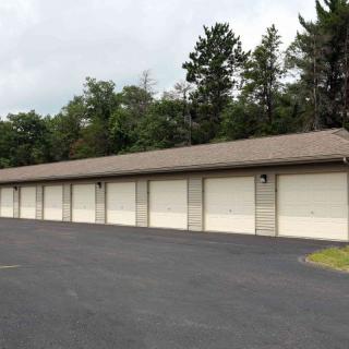 A row of outdoor storage units with closed garage doors on a paved lot.