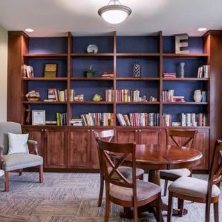 A cozy library corner with a wooden bookshelf, chairs, and a round table.