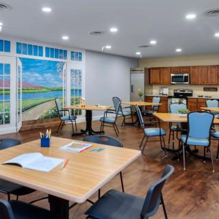 A well-lit classroom with multiple tables and chairs, featuring a kitchen area and a vibrant mural on the wall.