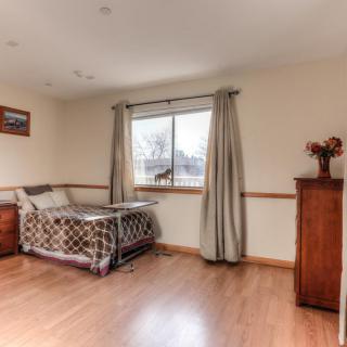 A cozy bedroom with a bed, wooden dresser, and large window with curtains.