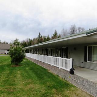 A spacious house with a long porch and white fence, surrounded by a green lawn and trees under an overcast sky.