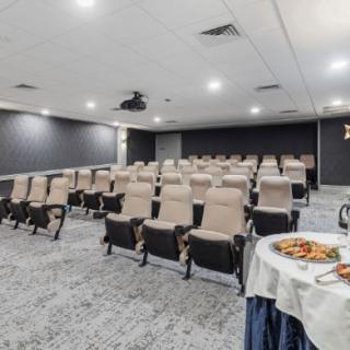 An empty theater-style room with rows of seats, a projector on the ceiling, and a table with food at the front.