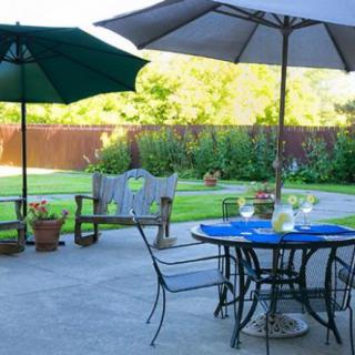 A cozy patio with outdoor seating, shaded by umbrellas, overlooking a lush garden.