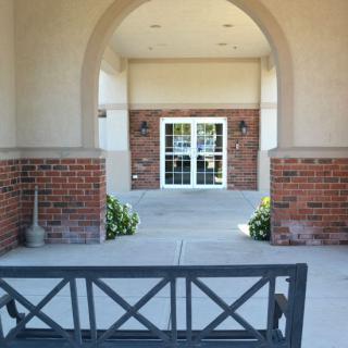 A bench positioned under an archway leading to a doorway with brick walls and plants on either side.