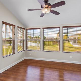 An empty room with large windows, hardwood floors, and a ceiling fan, overlooking an outdoor view.