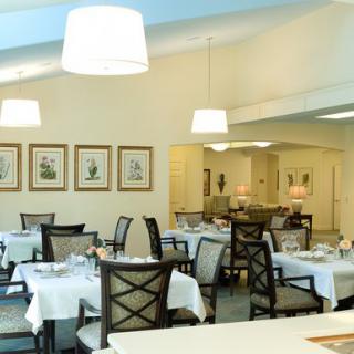 A well-lit dining room with elegantly arranged tables and chairs, featuring white tablecloths and framed artwork on the walls.