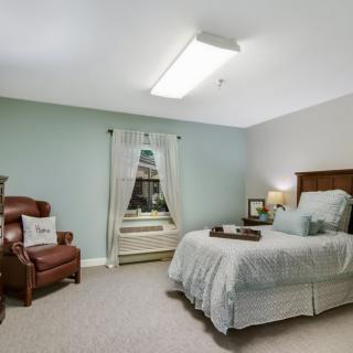 A cozy bedroom with a bed, a leather chair, and a window.