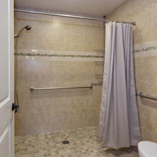 A bathroom with a walk-in shower featuring grab bars and a curtain.