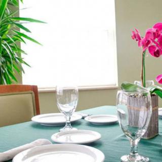 A neatly set dining table with white plates, glassware, and a pink orchid centerpiece.