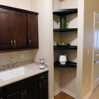 A modern kitchen area with dark wood cabinets, a sink, and decorative corner shelves.