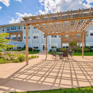 A beautiful outdoor patio area with a pergola and seating, adjacent to a modern building on a sunny day.