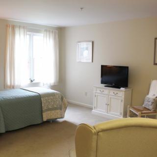 A cozy bedroom with a single bed, a TV, and a chair by the window.