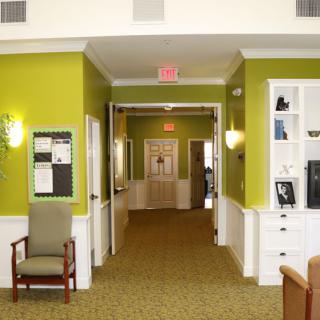 A well-lit hallway with green walls and carpeted flooring, featuring furniture and an exit sign.