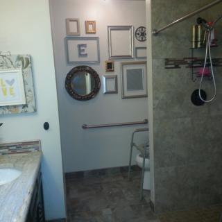 A bathroom featuring a shower with a towel rack, various wall art and mirrors, and a visible sink area.