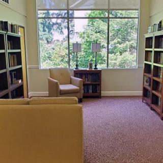 A cozy reading room with armchairs and bookshelves, featuring a large window overlooking greenery.