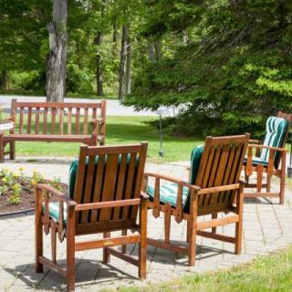 A peaceful garden patio with wooden chairs and a bench surrounded by greenery.