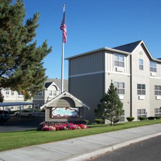 An apartment complex with an American flag and well-maintained landscaping on a clear day.