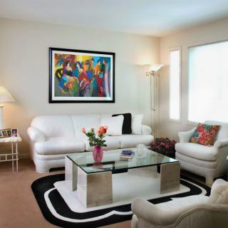A contemporary living room featuring white sofas, a glass coffee table, and vibrant wall art.