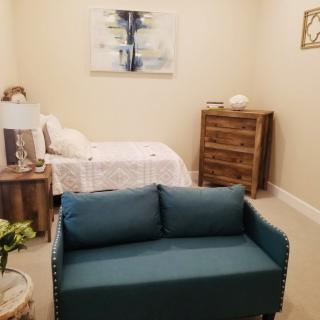 A cozy bedroom with blue sofa, bed, wooden dresser, and wall art.