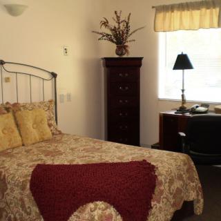 A cozy bedroom with a metal-framed bed, patterned bedding, and a tall dresser next to a window with light streaming in.