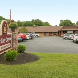 A single-story building with a parking lot in front, featuring several parked cars and a sign near the grass.