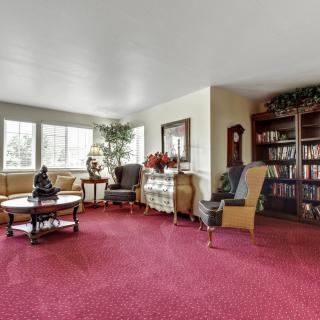 A spacious living room featuring a red carpet, comfortable seating, and a well-stocked bookshelf.
