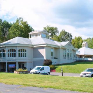 A large building with arched windows, surrounded by cars and greenery on a sunny day.
