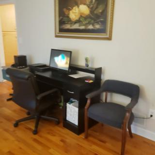 A home office setup with a computer desk, chair, monitor, and wall art.