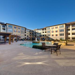 A modern apartment complex with a swimming pool and outdoor seating area under a clear blue sky.