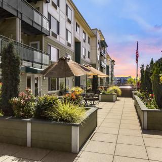 A modern apartment building with a well-maintained patio and lush green plants at sunset.