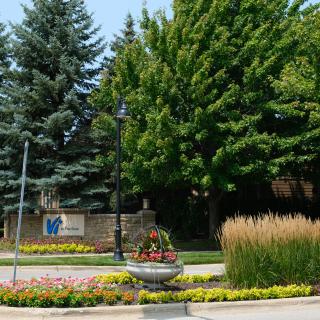 A scenic view of a landscaped area with lush trees, a decorative flower bed, and a lamp post.