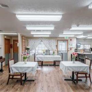 A well-lit dining room with tables and chairs, featuring wooden flooring and decorative curtains.