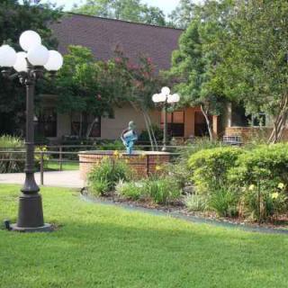 A serene garden scene with a lamp post, lush greenery, and a central statue.