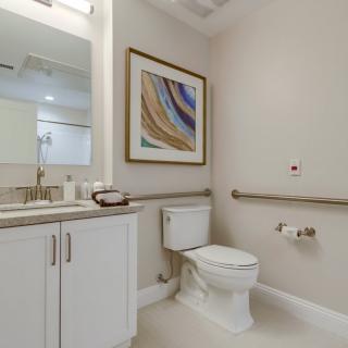 A modern bathroom with a toilet, sink, mirror, and contemporary artwork on the wall.
