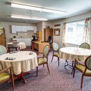 A cozy dining area with multiple round tables, chairs, and a small kitchen space in the background.